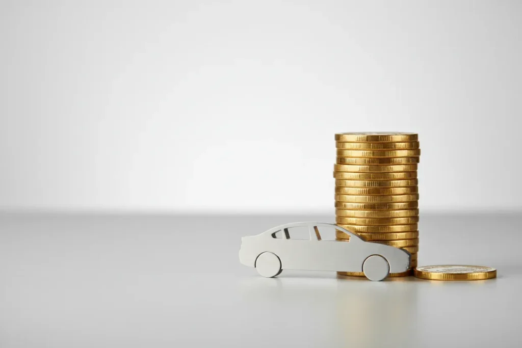 Stack of coins with a metal car silhouette on a soft gray background, plus an extra coin symbolizing early auto loan payoff.
